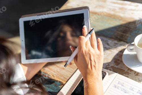 Preview: Woman holding a digital tablet with empty black screen while working sitting in a coffee shop.
