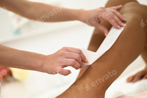 Preview: Woman having hair removal procedure on leg applying wax strip depilatory in salon. Depilation