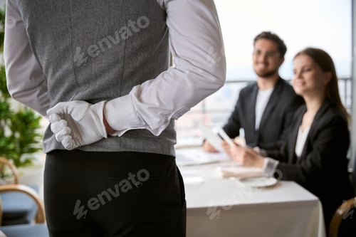 Preview: Waiter holds his hand behind his back while taking an order from a young couple