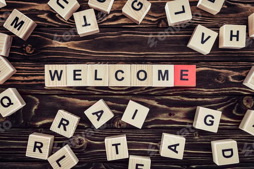 Preview: flat lay with wooden cubes arranged in welcome word on brown wooden surface