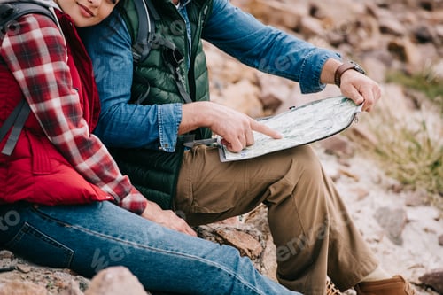 Preview: partial view of hikers with map sitting on rocks on sandy beach
