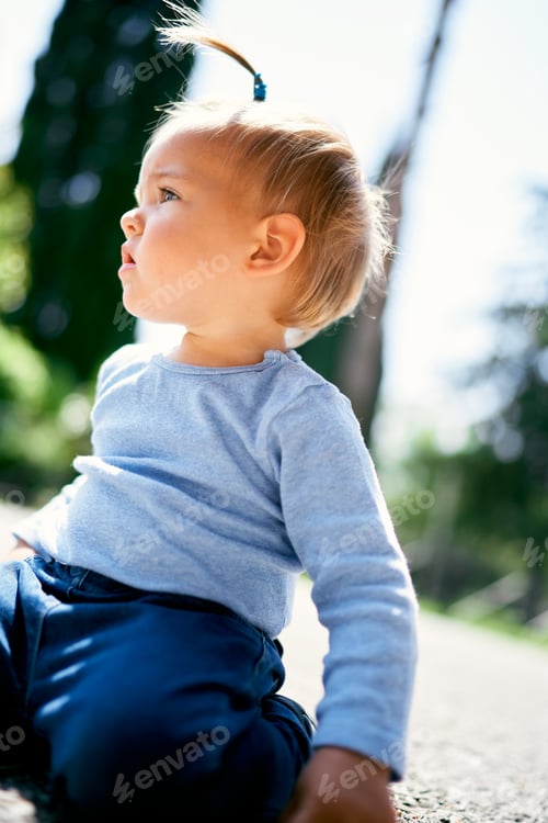 Preview: Little girl with a ponytail sits on her knees on the road. Close-up