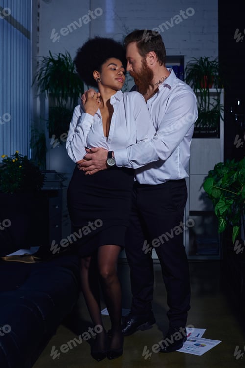 Preview: full length of stylish interracial couple in formal wear embracing in office, romantic encounter