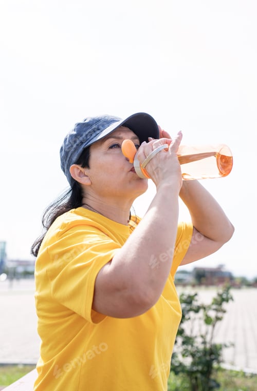 Preview: Smiling senior woman drinking water after workout outdoors on the sports ground
