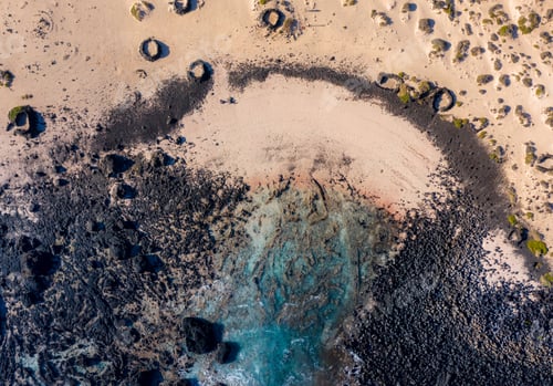 Preview: the turquoise ocean forms a small bay on the black-red-yellow beach