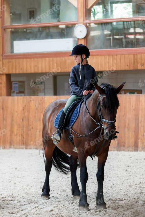 Preview: Horse riding school. Little children girls at group training equestrian lessons in indoor ranch