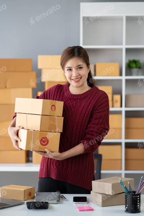 Preview: Smiling Asian small business owner holding boxes, preparing her products for her customer.