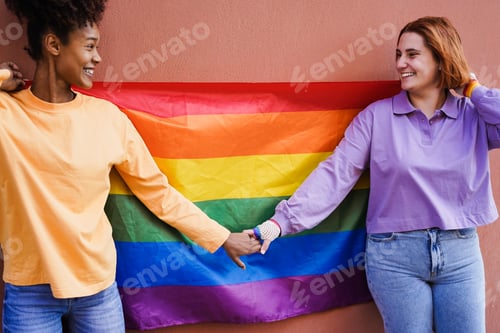 Preview: Happy women gay couple holding rainbow flag outdoor - Focus on right lesbian girl face