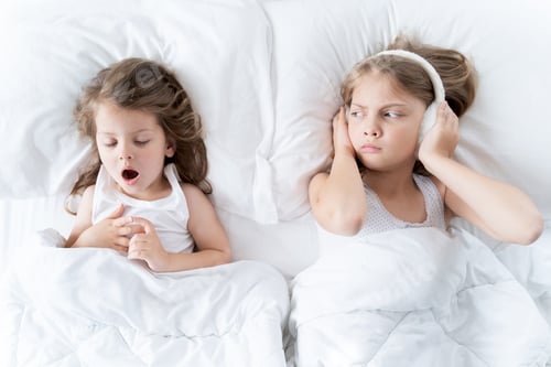 Preview: Little girls sleep in bed. One is snoring hard,sister is plugging ears with fur headphones.Early mor