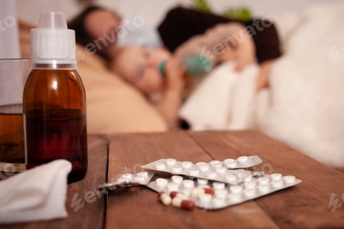 Preview: Dad and daughter get sick on the bed against the background of pills and medicines. A man wearing a