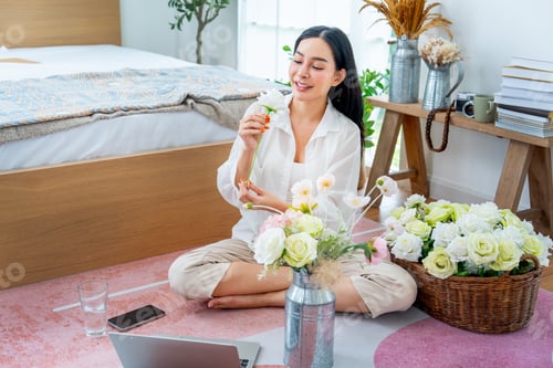 Preview: High view of beautiful Asian woman sit on the floor with happiness to flower arrangement in bedroom