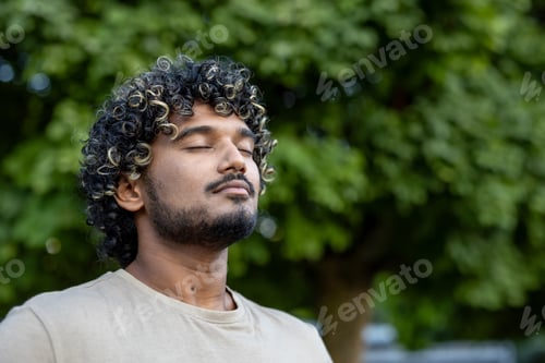 Preview: A serene portrait of a man with curly hair enjoying a peaceful moment outside surrounded by green