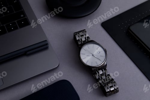 Preview: Business layout of a fragment of a laptop, charger, phone and stylish wristwatch close-up on a gray