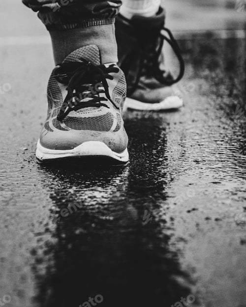 Preview: Vertical grayscale closeup shot of a man in a pair of sports running shoes walking on the wet ground