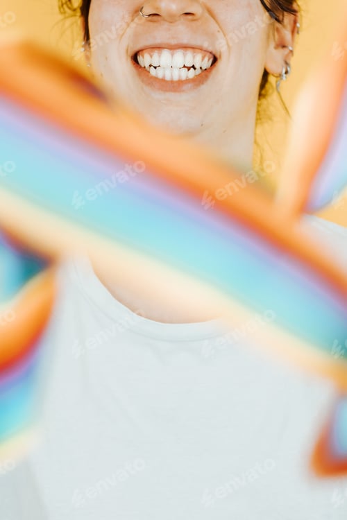 Preview: Young woman smiling happily to camera while holding a LGBTIQ flag waving to camera.
