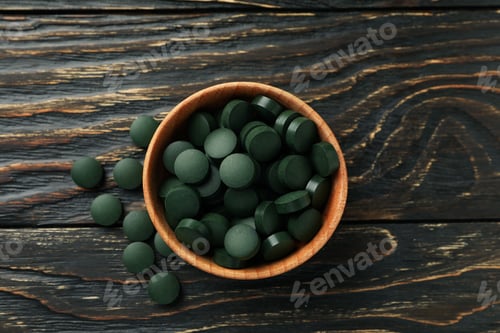 Preview: Wood bowl with spirulina pills on wooden background, top view