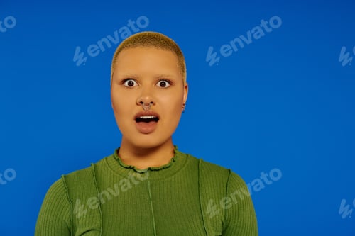 Preview: A stylish young woman expresses surprise against a vibrant blue background in an artistic setting