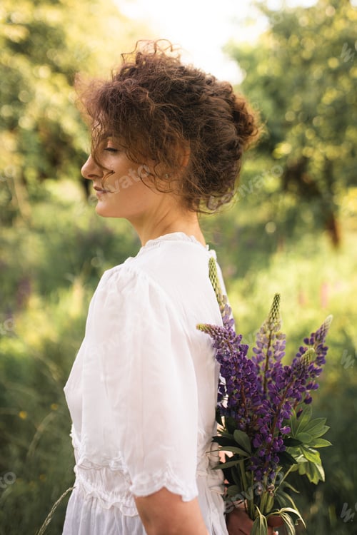 Preview: Girl in a field with lupines. Beautiful girl enjoys summer. Summer mood. Romantic mood. Curly girl.
