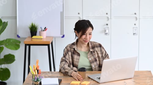 Preview: Smiling young woman designer working with laptop in modern workplace.