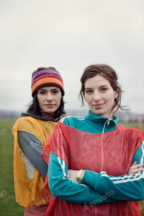 Preview: Portrait of two Caucasian women in sports clothing with team bibs of opposing teams and woolly hats