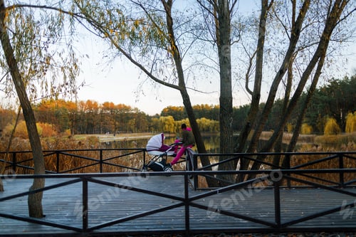 Preview: young mother sitting in park and mesagging wih smartphone while her baby sleep in stroller. Girl sit