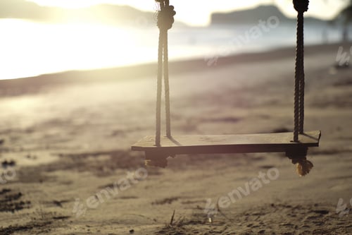 Preview: Closeup old wooden swing hanging from the branch of tree on the beach