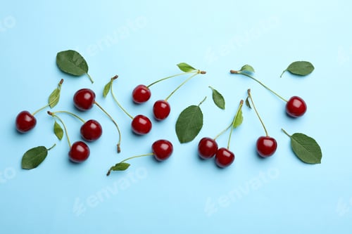 Preview: Tasty ripe cherries with leaves on light blue background, flat lay