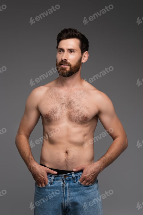 Preview: shirtless and bearded man with hair on chest posing with hands in pockets isolated on grey