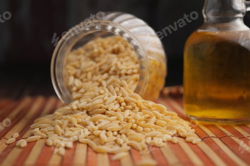 Preview: Pine nuts spill from a jar beside oil on a wooden mat