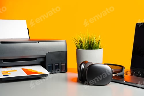 Preview: Laser printer and laptop on desk against yellow background