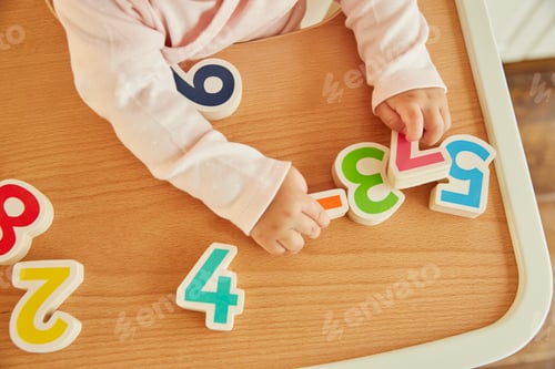 Preview: Overhead cropped view of baby girl playing with toy numerals on high chair