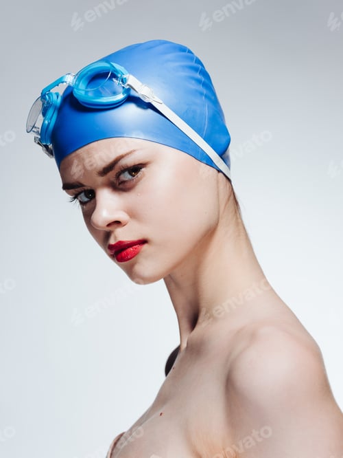 Preview: Woman in a cap and goggles for swimming on a light background naked shoulders red lips