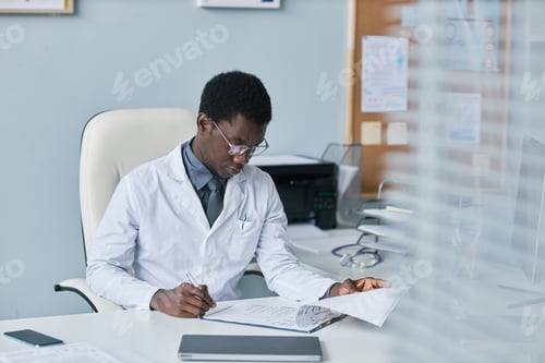 Preview: Young black doctor filling papers at desk in office working in clinic