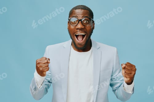 Preview: Excited man celebrating success with joy in a light blue setting, wearing glasses and a blazer