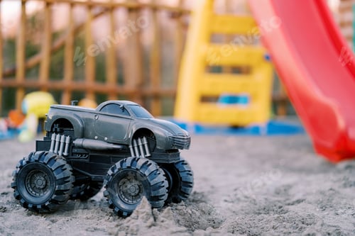 Preview: Toy Bigfoot jeep stands on the sand at a colorful playground