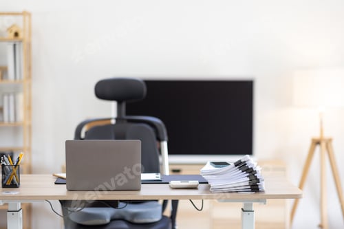 Preview: Laptop Computer, notebook, and eyeglasses sitting on a desk in a large open plan office space after