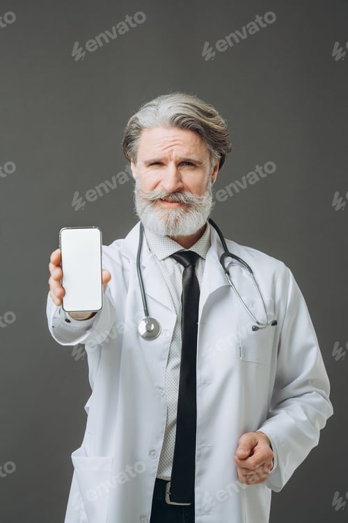 Preview: A gray-haired doctor in a white medical coat shows the phone screen to the camera. Medicine mockup.