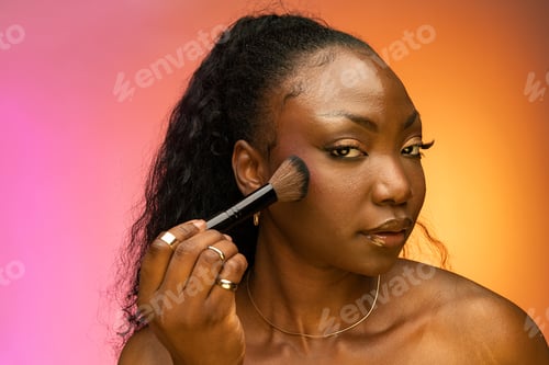 Preview: Beautiful African American woman applying powder and blush, isolated on colorful background