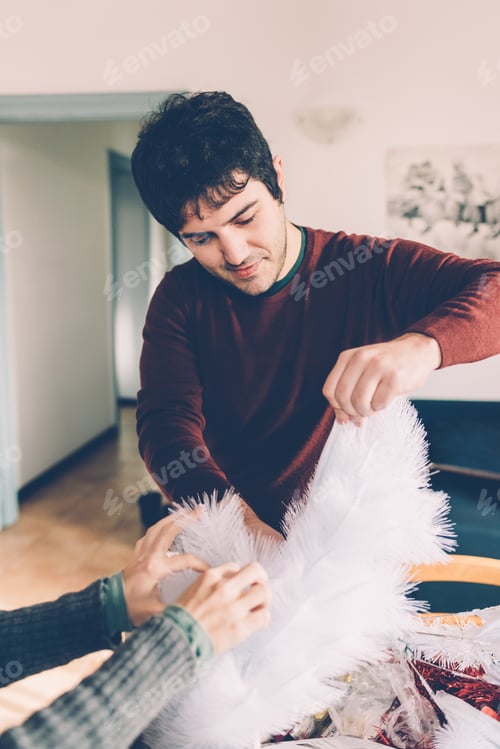 Preview: Young couple at home decorating xmas tree