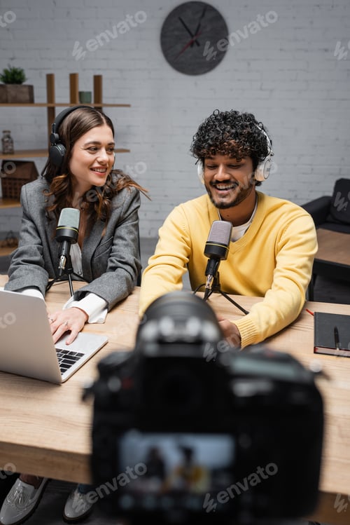 Preview: bearded indian man in headphones and yellow jumper talking in microphone near notebook and smiling