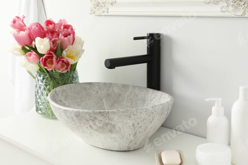Preview: Vase with beautiful pink tulips and toiletries near sink in bathroom