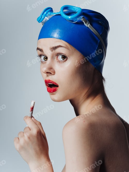 Preview: Woman swimmer in a blue swimming cap is smoking on a light background