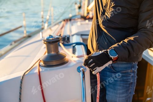 Preview: Young man captain operates and controls a sailboat during a journey by sea in winter time in