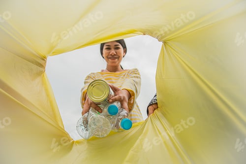 Preview: Volunteer asian woman throws plastic bottles and metal cans into garbage bags for recycling