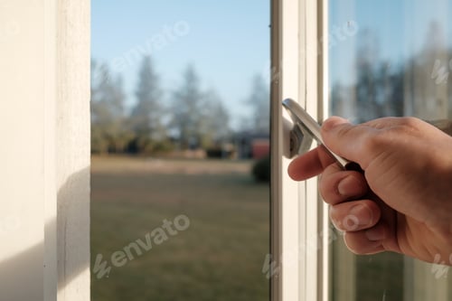Preview: Hand opens a metal latch on the frame of a white wooden window, indoors.