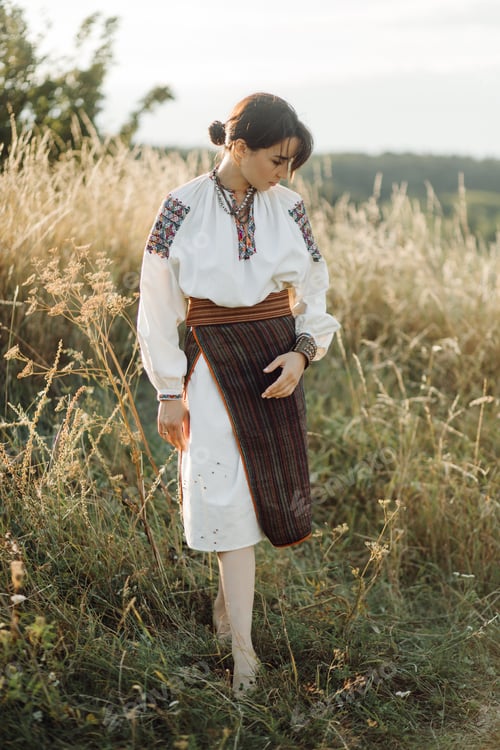 Preview: Young woman in traditional national embroidered shirt and skirt on nature at sunset.