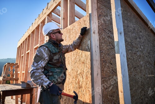 Preview: Carpenter hammering nail into OSB panel while building wooden frame house.