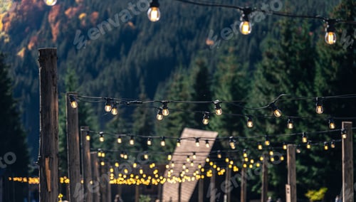 Preview: Decorative light bulbs on wooden poles in a mountainous area.