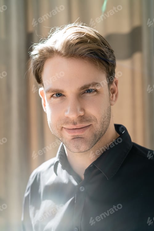 Preview: young man in black shirt smiling at camera in sunshine at home