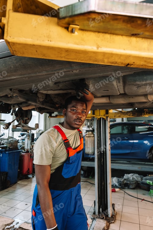 Preview: Young African mechanic in uniform working under the car in car service center
